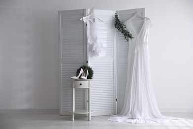 Photo of Wedding dress, high heel shoes and veil near white wall indoors