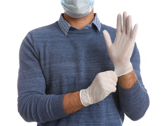 Man in protective face mask putting on medical gloves against white background, closeup