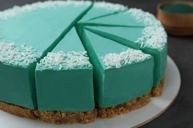 Photo of Sliced tasty spirulina cheesecake on dark grey table, closeup view