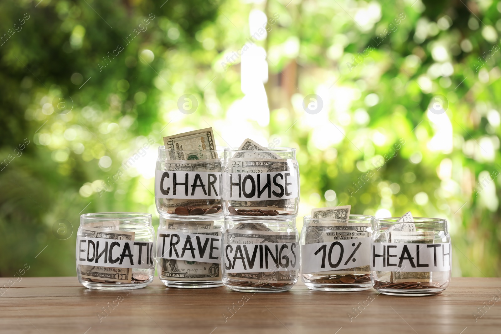 Photo of Glass jars with money for different needs on table against blurred background