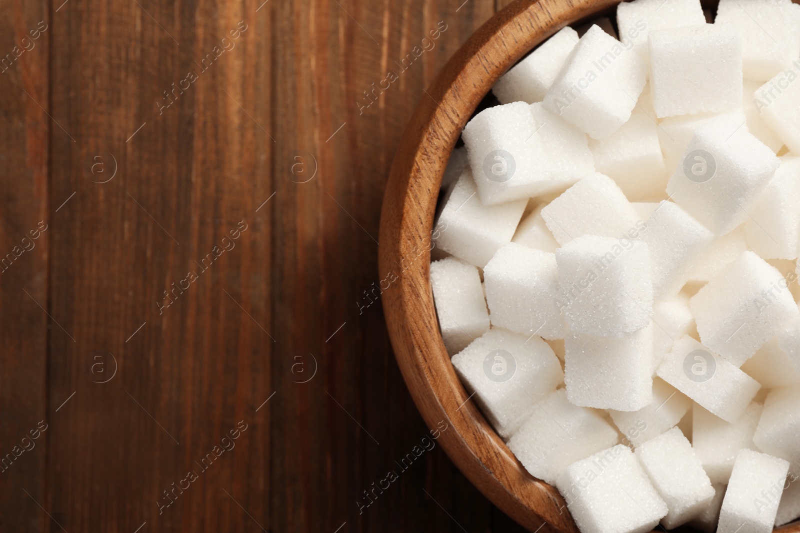 Photo of Bowl with sugar cubes on wooden table, top view. Space for text