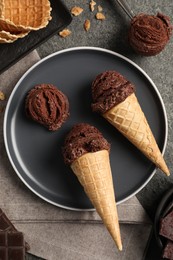 Photo of Chocolate ice cream scoops in wafer cones on gray textured table, flat lay