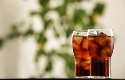 Glasses with cola and ice cubes on table against blurred background. Space for text