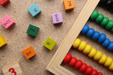 Photo of Wooden cubes with numbers and multiplications near abacus on fiberboard, flat lay