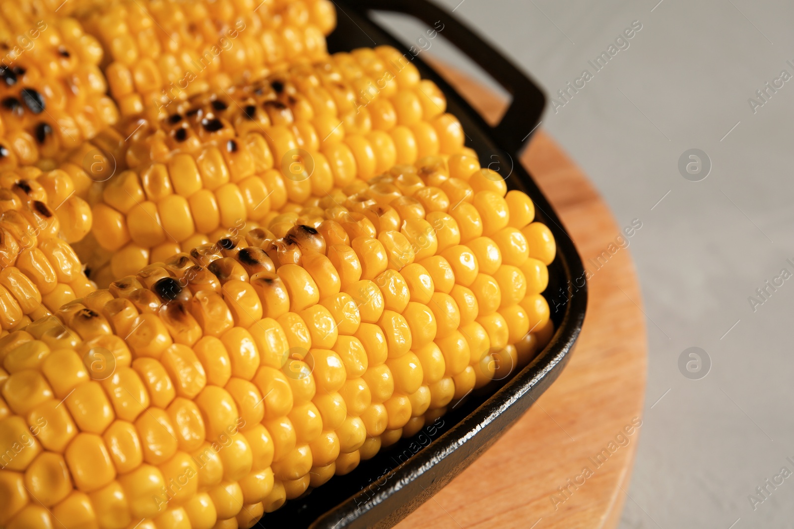 Photo of Fresh grilled tasty corn cobs in pan on light background, closeup