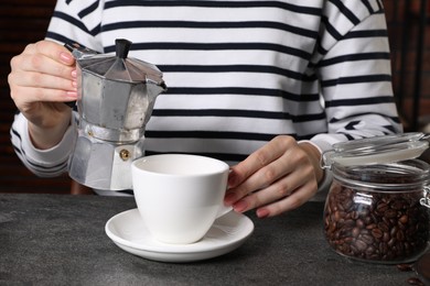 Photo of Woman pouring aromatic coffee from moka pot into cup at grey table indoors, closeup