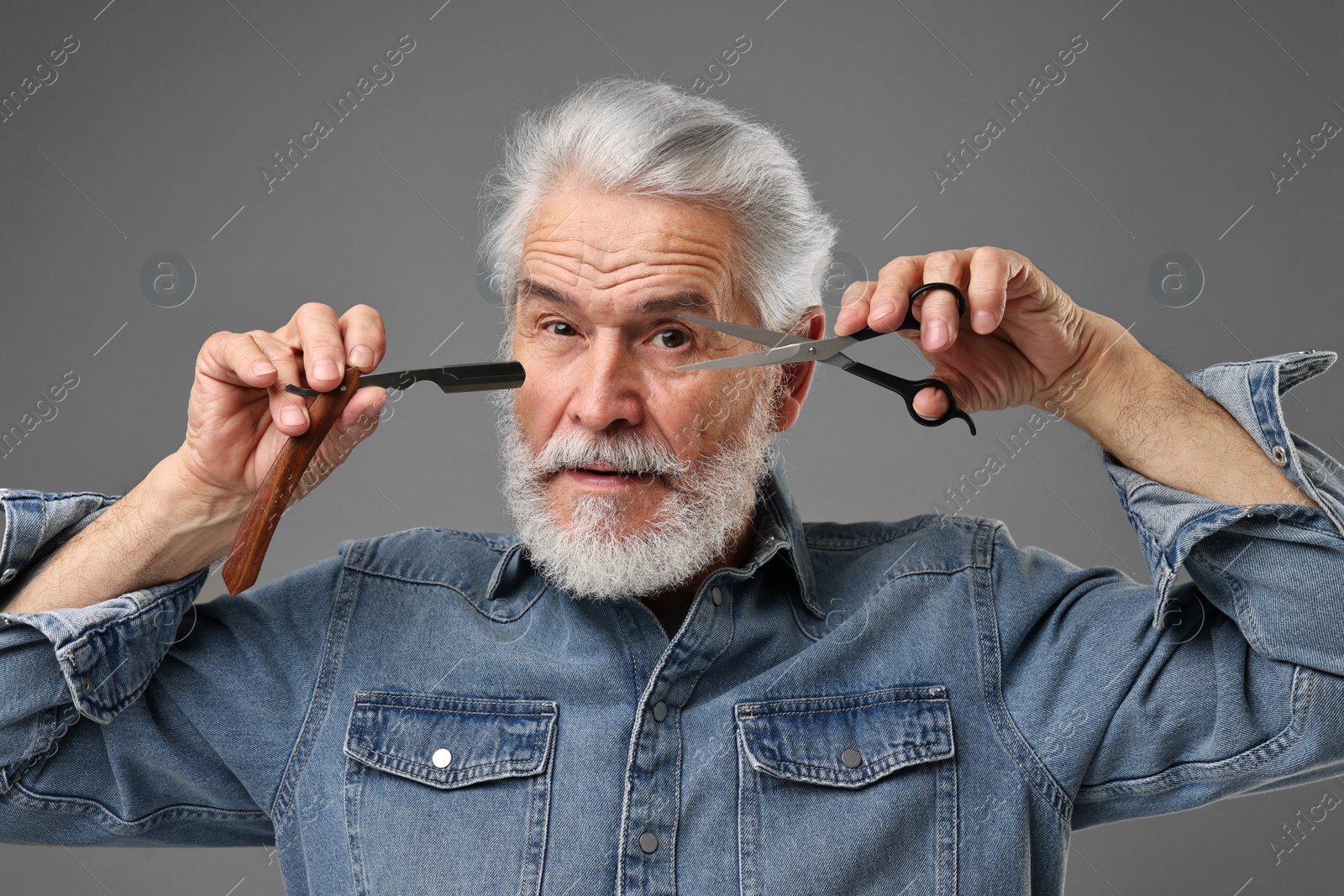 Photo of Senior man with mustache holding blade and scissors on grey background