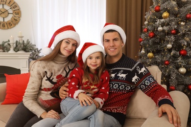 Happy family in Santa hats near Christmas tree at home