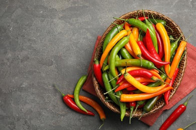 Photo of Wicker bowl with different chili peppers on grey table, flat lay. Space for text