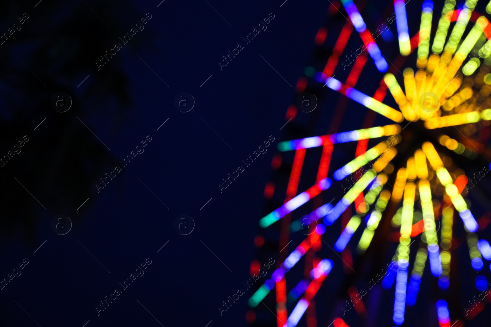 Photo of Blurred view of beautiful glowing Ferris wheel against dark sky. Space for text