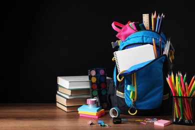 Photo of Backpack with different school stationery on wooden table near blackboard, space for text