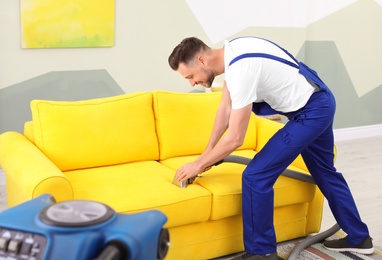 Dry cleaning worker removing dirt from sofa indoors