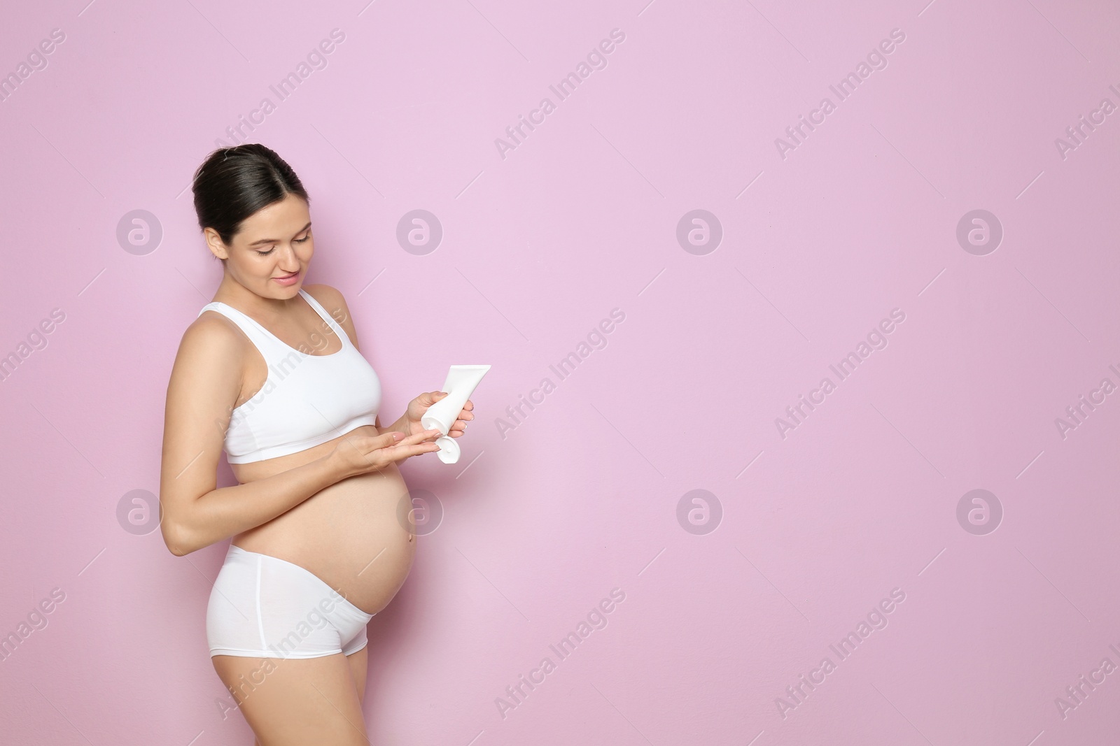 Photo of Pregnant woman holding body cream on color background with space for text