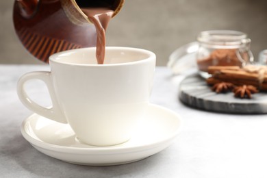 Photo of Pouring tasty hot chocolate into cup at light table, closeup. Space for text