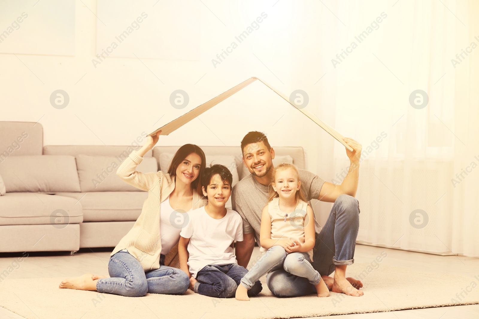 Image of Happy family sitting under cardboard roof at home. Insurance concept