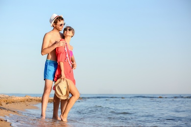 Happy young couple near water on beach. Space for text