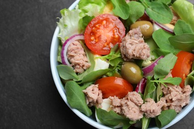 Photo of Bowl of delicious salad with canned tuna and vegetables on black table, top view