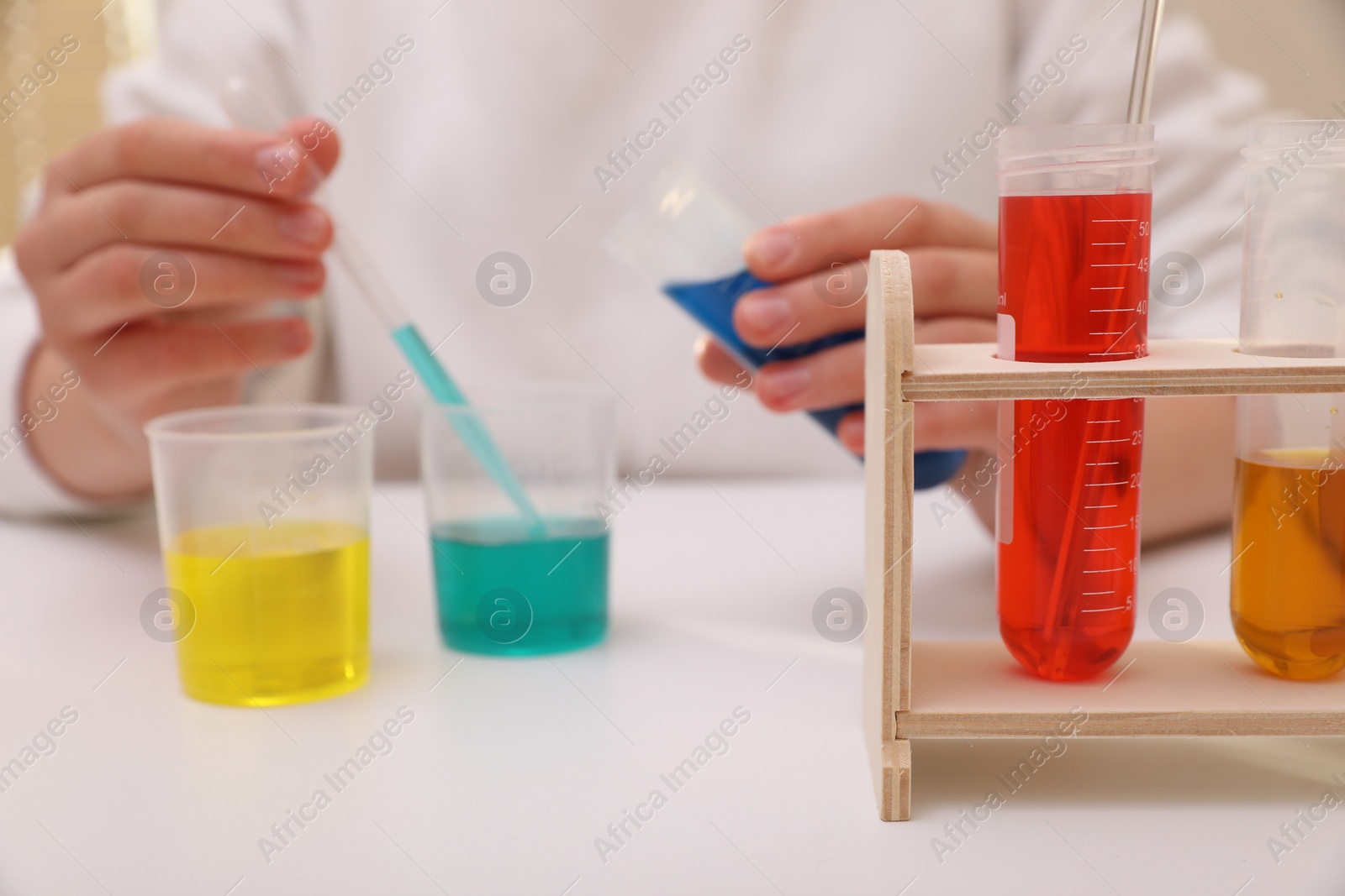 Photo of Girl mixing colorful liquids at white table indoors, selective focus. Kids chemical experiment set