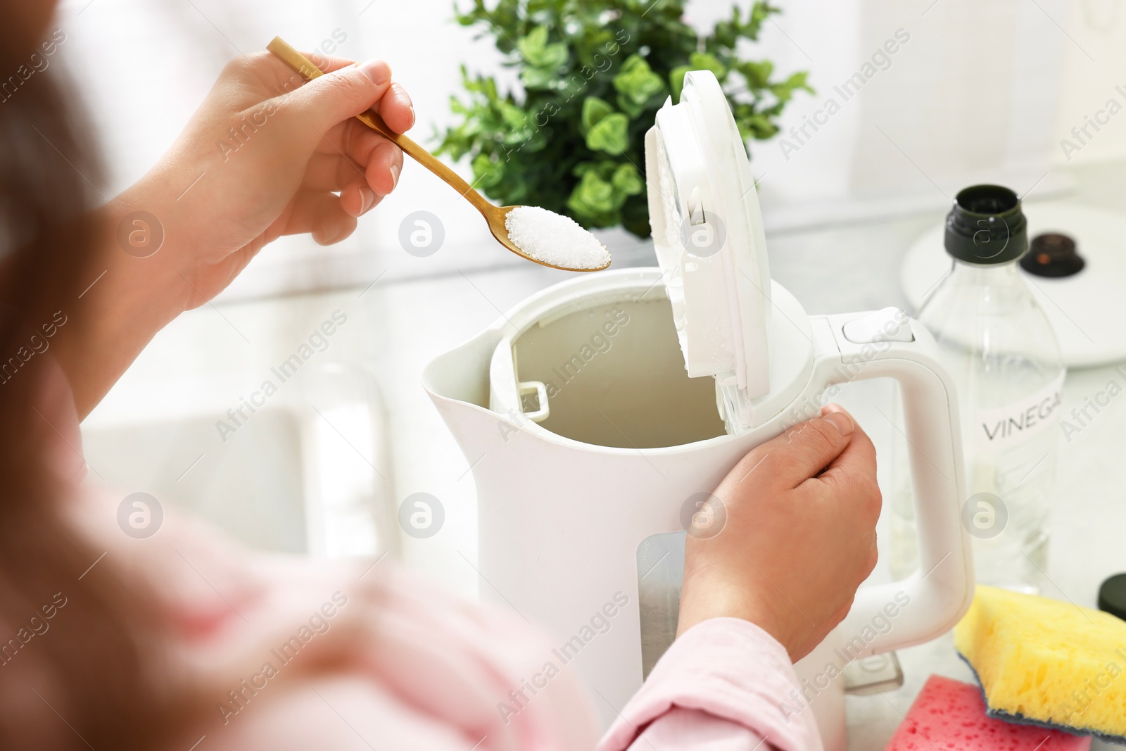Photo of Woman adding baking soda into electric kettle in kitchen, closeup