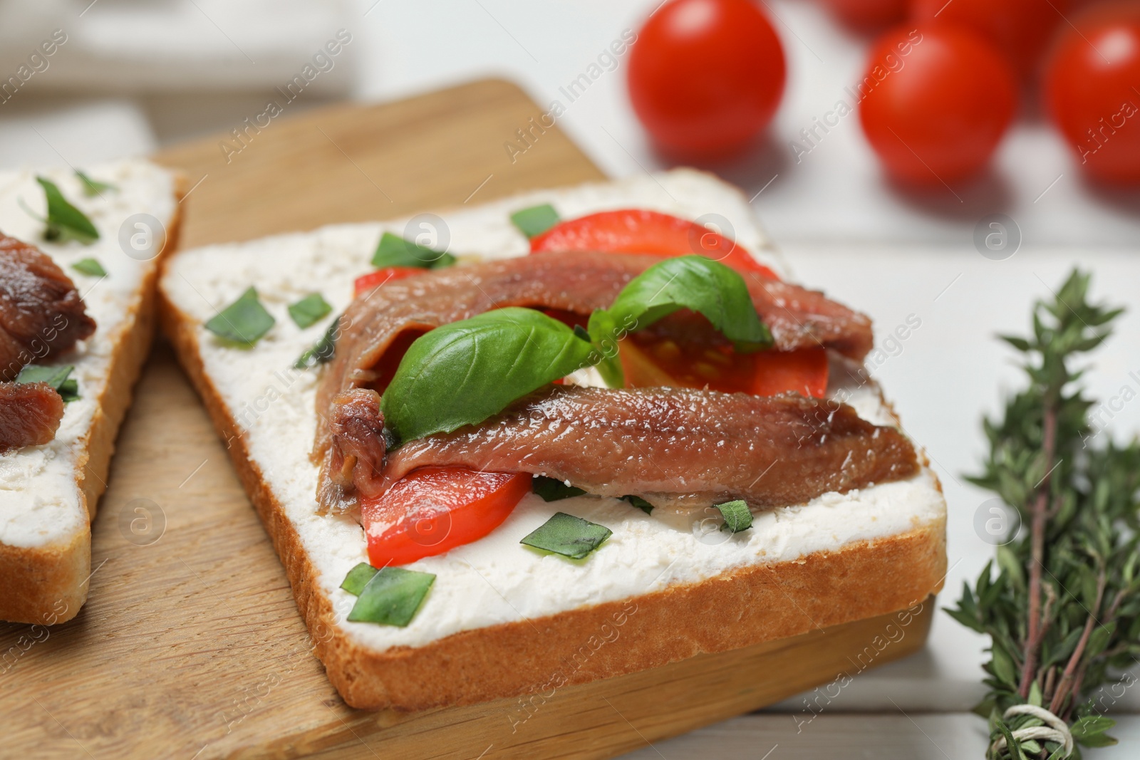 Photo of Delicious sandwiches with cream cheese, anchovies, tomatoes and basil on white wooden table, closeup