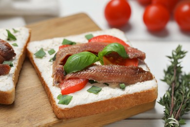 Delicious sandwiches with cream cheese, anchovies, tomatoes and basil on white wooden table, closeup