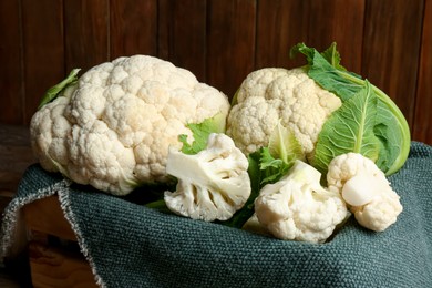 Photo of Crate with cut and whole cauliflowers on wooden table, closeup