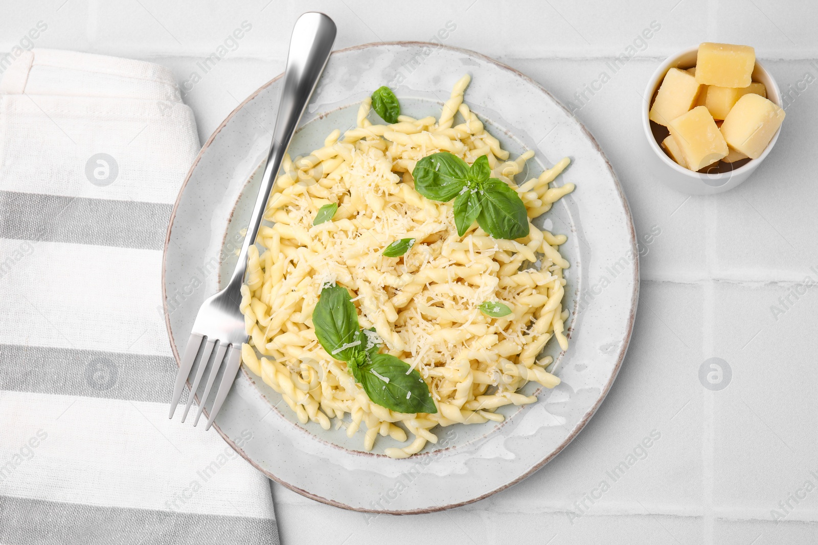 Photo of Plate of delicious trofie pasta with cheese and basil leaves served on white tiled table, flat lay