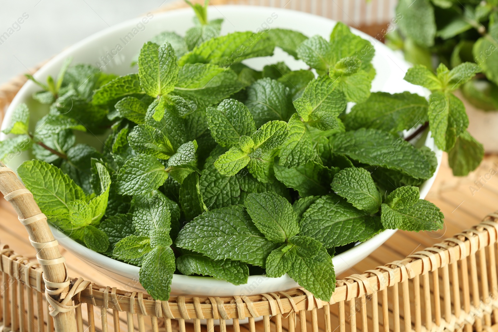 Photo of Bowl of fresh green mint leaves on wicker tray, closeup