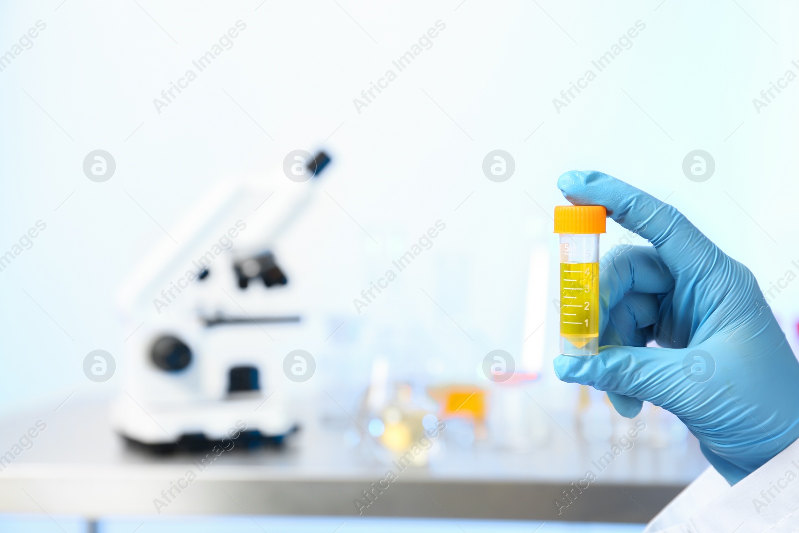 Photo of Laboratory assistant holding urine sample in container indoors, closeup with space for text. Medical analysis