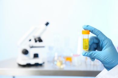 Laboratory assistant holding urine sample in container indoors, closeup with space for text. Medical analysis