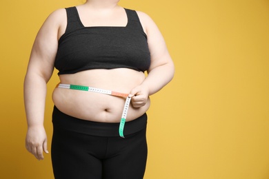 Overweight woman with measuring tape on color background