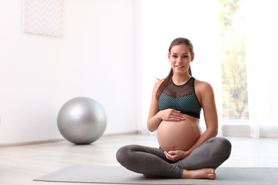 Photo of Young pregnant woman in fitness clothes at home. Space for text