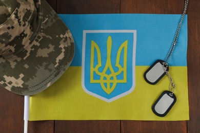 Photo of MYKOLAIV, UKRAINE - SEPTEMBER 26, 2020: Military cap, ID tags and Ukrainian flag on wooden table, flat lay