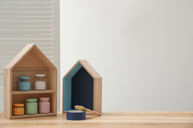 Photo of House shaped shelf brush and jars of paints on table. Space for text