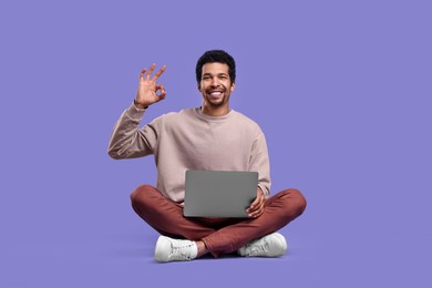 Happy man with laptop showing ok gesture on purple background