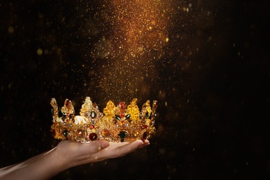 Image of Fantasy world. Woman holding beautiful golden crown lit by magic light, closeup