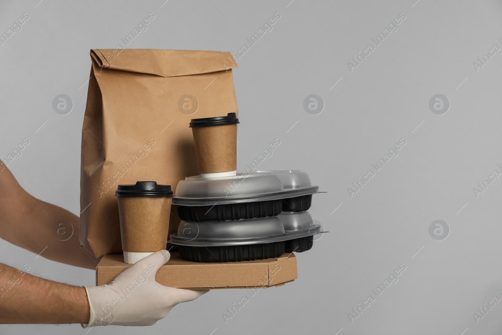 Photo of Courier in protective gloves holding order on light grey background, closeup. Food delivery service during coronavirus quarantine