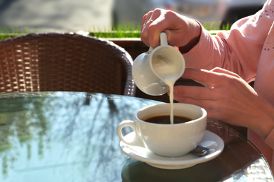 Woman pouring milk in coffee at table in cafe