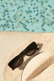 Stylish hat and sunglasses near outdoor swimming pool on sunny day, top view. Space for text
