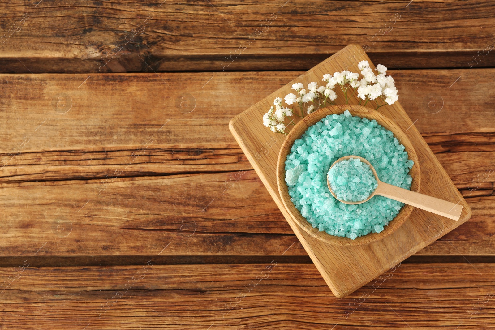 Photo of Turquoise sea salt and beautiful flowers on wooden table, top view. Space for text