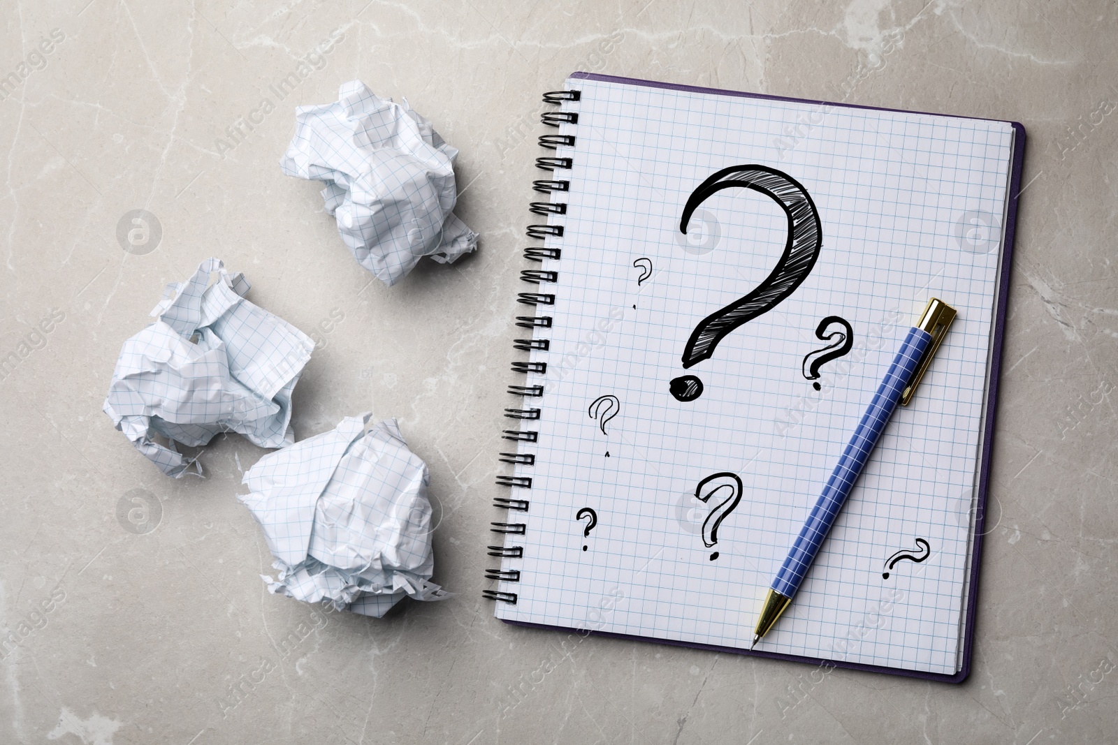 Image of Notebook with question marks, pen and crumpled paper balls on grey marble table, flat lay