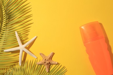 Photo of Sunscreen, sea stars and tropical leaves on yellow background, flat lay and space for text. Sun protection care