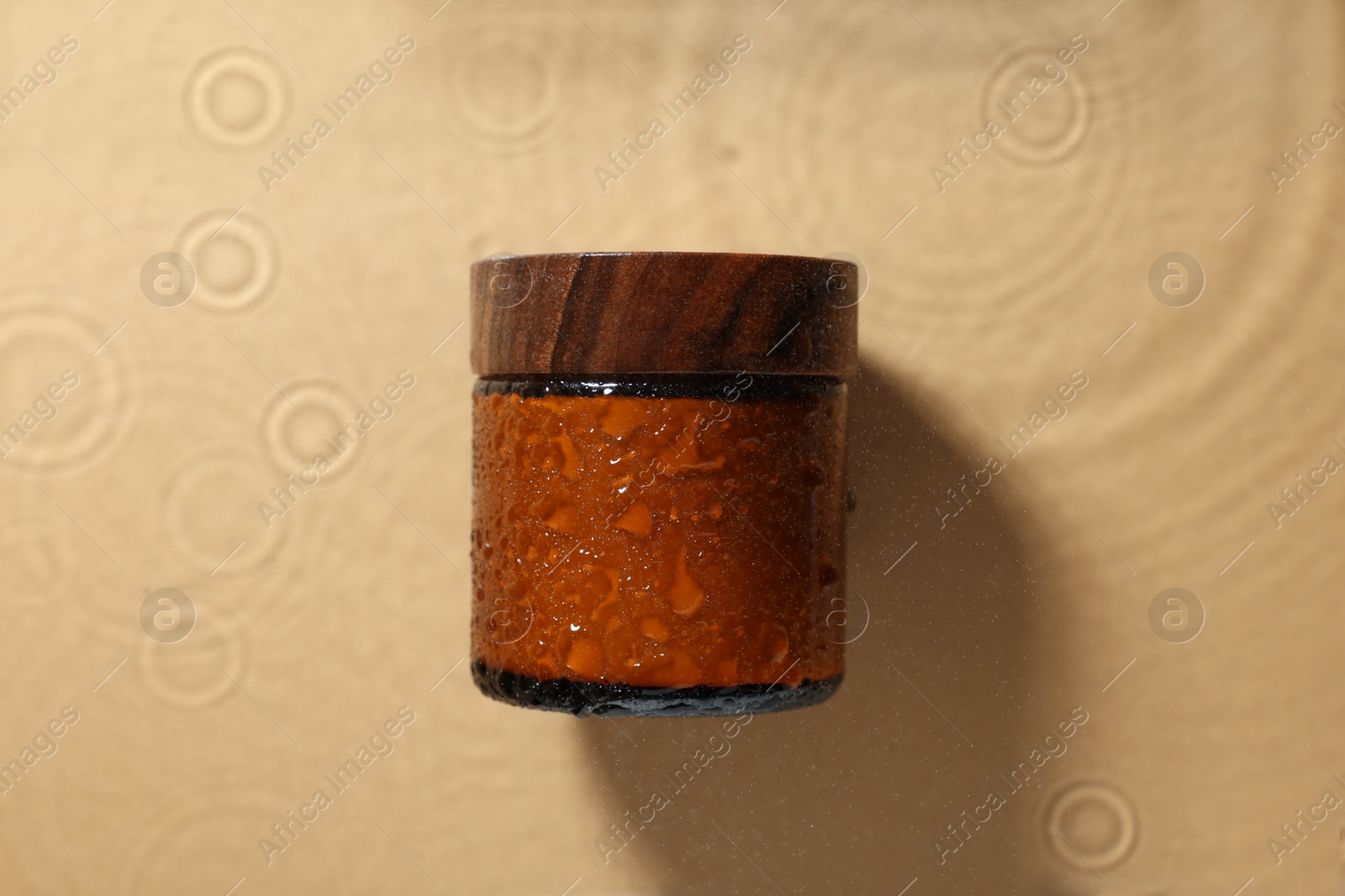 Photo of Jar of cosmetic product in water on beige background, top view