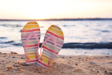 Stylish flip flops on sand near sea, space for text. Beach accessories