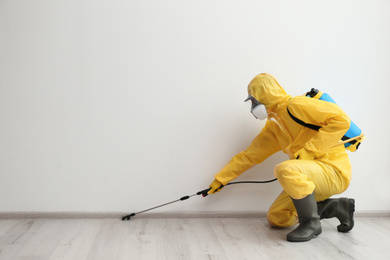 Pest control worker in protective suit spraying pesticide indoors. Space for text