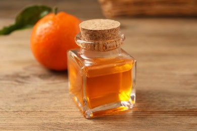 Bottle of tangerine essential oil and fresh fruit on wooden table, closeup