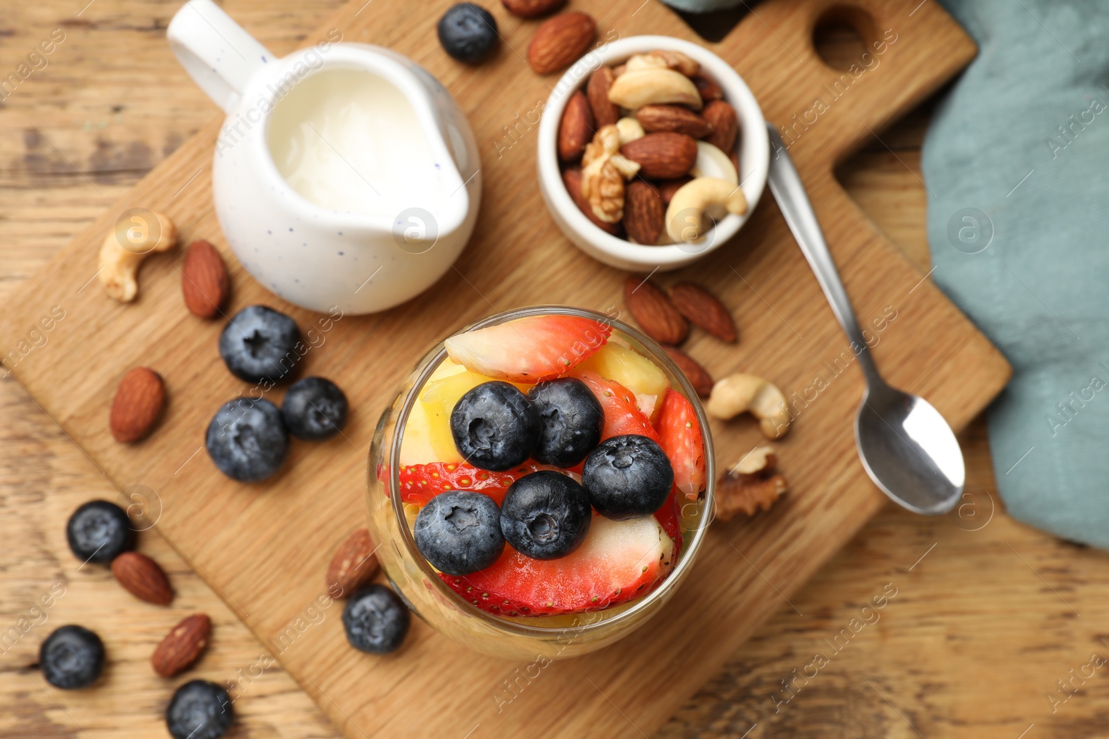 Photo of Delicious fruit salad, berries and nuts on wooden table, flat lay