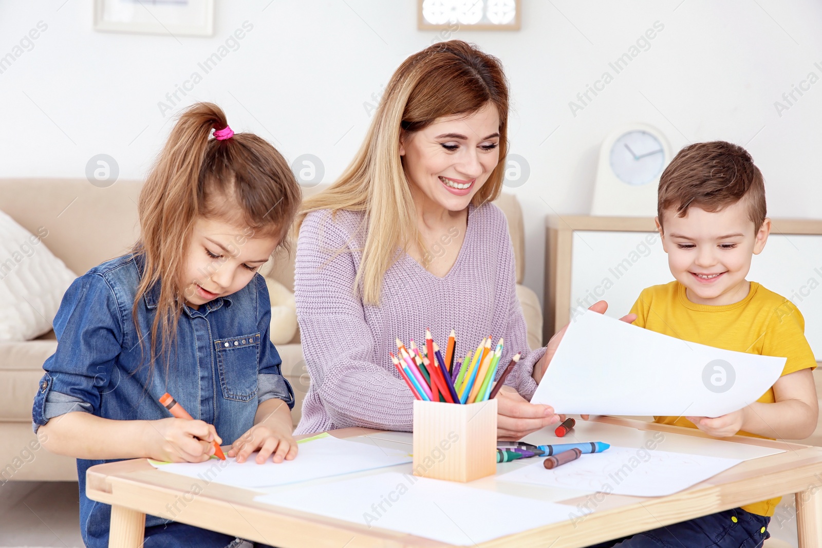 Photo of Cute little children and their nanny drawing at home