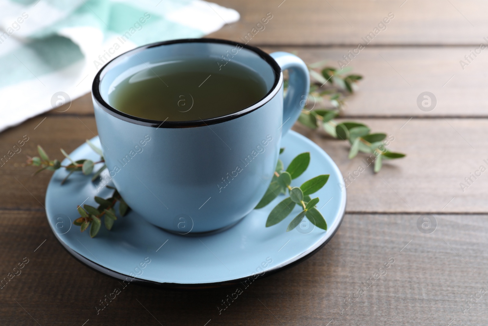 Photo of Cup of green tea and eucalyptus leaves on wooden table. Space for text