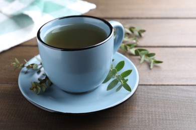 Photo of Cup of green tea and eucalyptus leaves on wooden table. Space for text